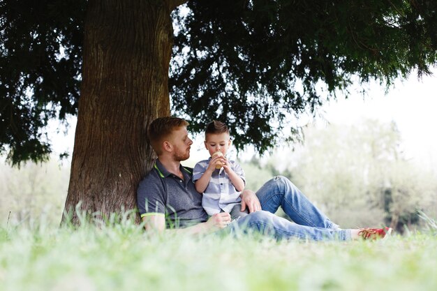 Vrolijke vader en zoon hebben plezier spelen onder de boom in het park