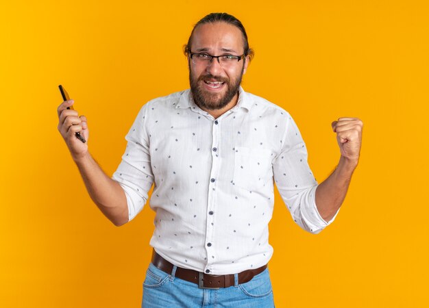 Vrolijke volwassen knappe man met een bril die een mobiele telefoon vasthoudt en een ja-gebaar doet