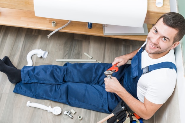 Vrolijke volwassen loodgieter zitten in de badkamer