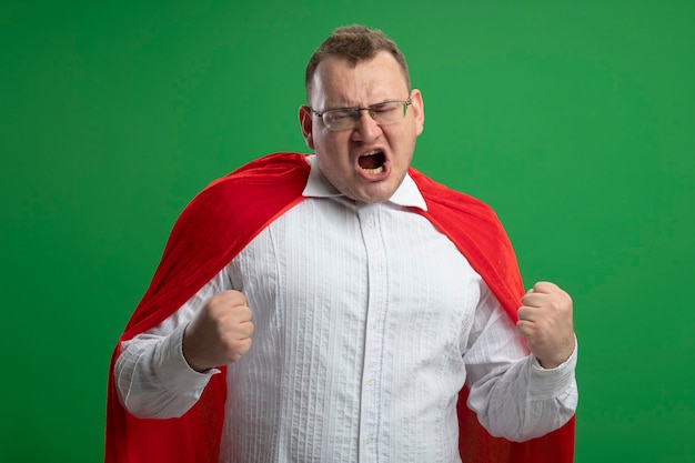 Vrolijke volwassen Slavische superheld man in rode cape bril doen ja gebaar geïsoleerd op groene muur