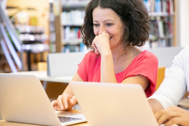 Vrolijke volwassen student die van inhoud op computer geniet