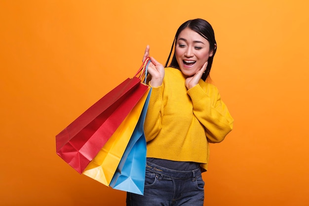 Vrolijke vriendelijke modieuze shopper die lacht terwijl hij boodschappentassen draagt en een gele trendy trui draagt. Dolblije opgewonden mooie klant die zich glamoureus en zelfverzekerd voelt.