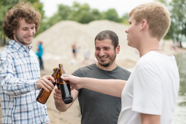 Gratis foto vrolijke vrienden die flessen op strand clinking