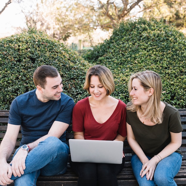 Gratis foto vrolijke vrienden die laptop in park met behulp van