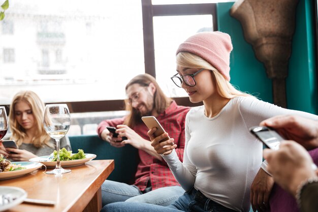 Vrolijke vrienden zitten in café met behulp van mobiele telefoons.