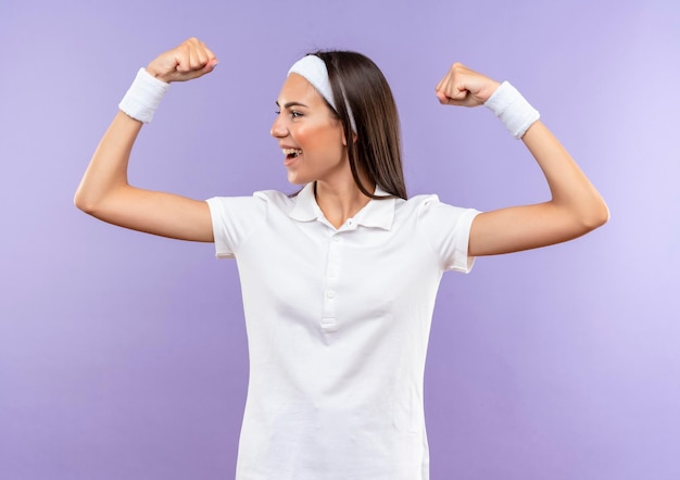 Vrolijke, vrij sportieve meid met een hoofdband en een polsband die sterk gebarend naar de kant geïsoleerd op een paarse muur