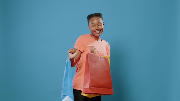 Vrolijke vrouw die danst en boodschappentassen vasthoudt na betaling in de winkel. gelukkige persoon die kleren in kleurrijke paperbags koopt en aankoop voor camera toont.