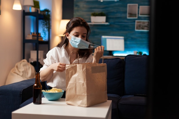 Vrolijke vrouw die een gezichtsmasker voor medische bescherming neemt na het kopen van afhaalmaaltijden