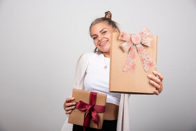 Vrolijke vrouw die geschenkdozen op grijze backround toont.