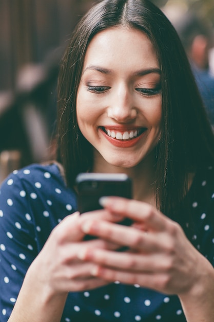 Vrolijke vrouw die haar mobiele telefoon met beide handen