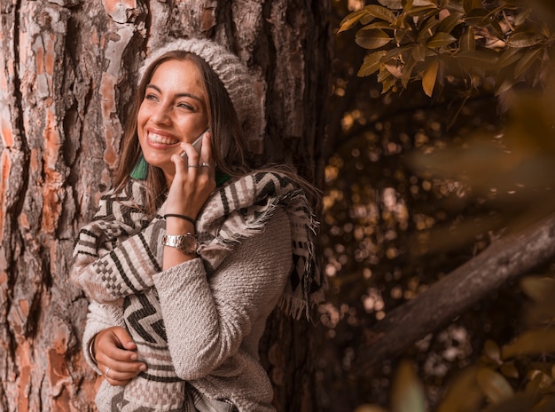 Vrolijke vrouw die telefoongesprek heeft dichtbij boom