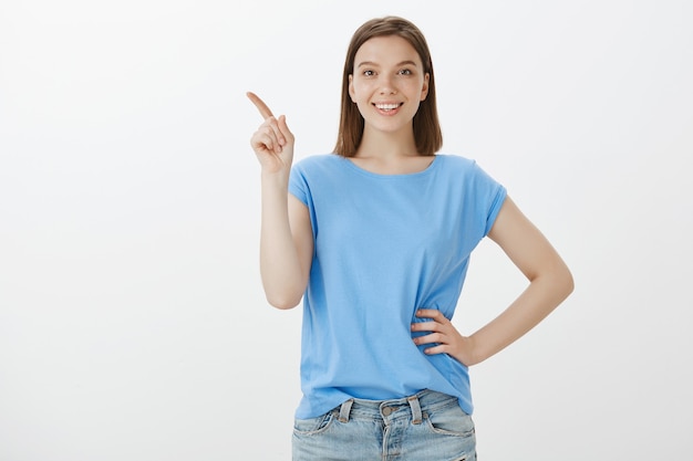 Vrolijke vrouw in blauw t-shirt die linksboven wijst en je logo laat zien
