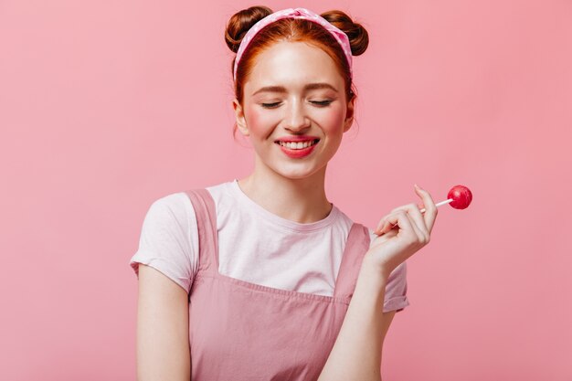 Vrolijke vrouw in wit T-shirt en top glimlacht en houdt snoep op roze achtergrond.