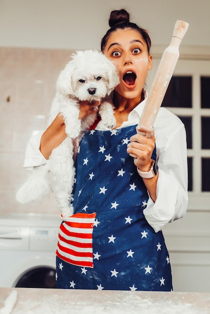 Gratis foto vrolijke vrouw met een deegroller en witte maltese hond