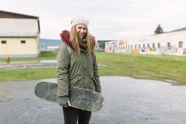 Vrolijke vrouw met skateboard die camera bekijken