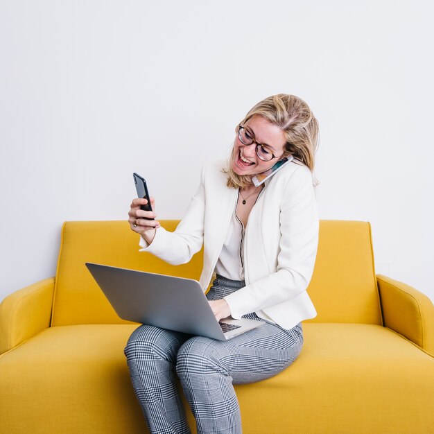 Vrolijke vrouw met smartphones die laptop met behulp van