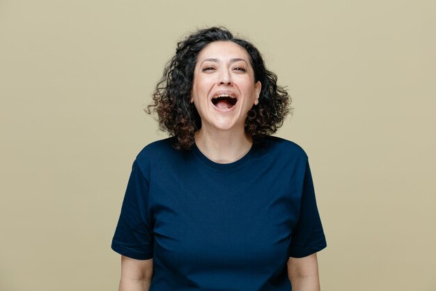 Vrolijke vrouw van middelbare leeftijd die een t-shirt draagt en naar een camera kijkt die lacht geïsoleerd op een olijfgroene achtergrond