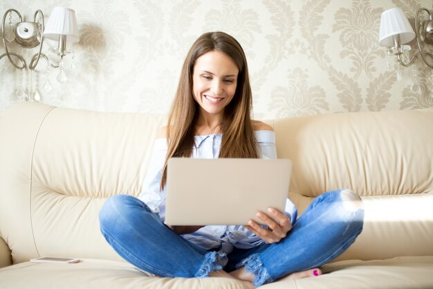 Vrolijke vrouw zittend op de bank en met behulp van touchpad