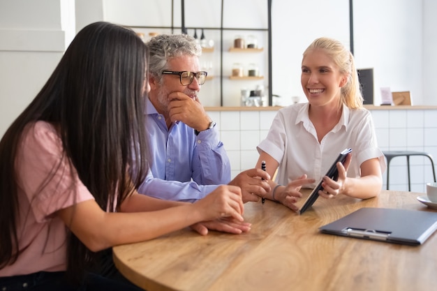 Vrolijke vrouwelijke manager en jonge en volwassen klanten kijken en bespreken presentatie op tablet, glimlachen en praten