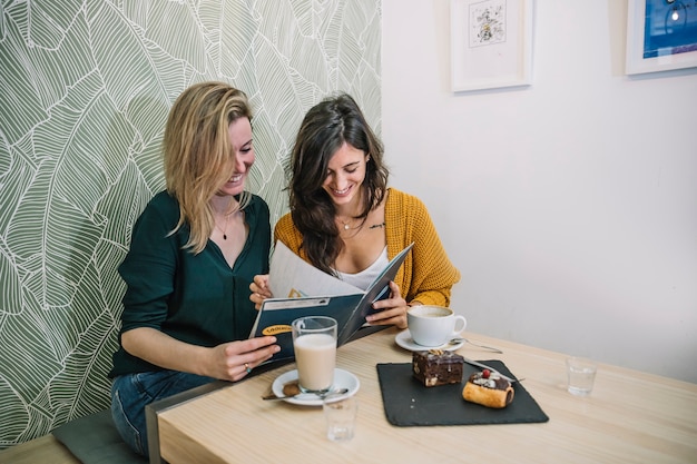 Vrolijke vrouwen die menu in koffie lezen