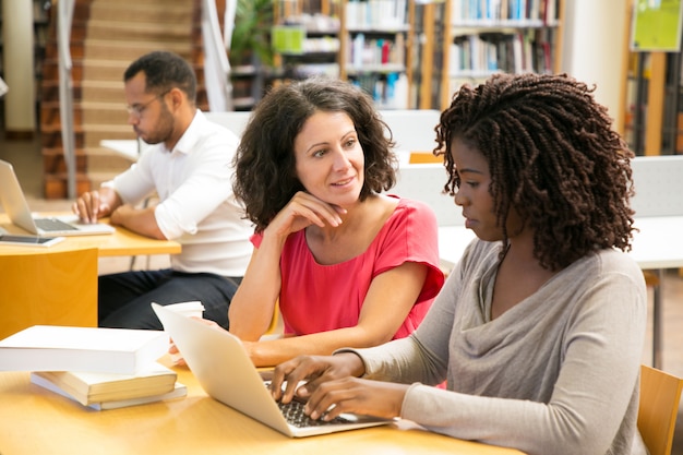 Vrolijke vrouwen die met laptop bij openbare bibliotheek werken