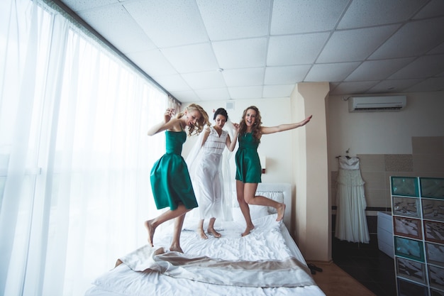 Vrolijke vrouwen springen op bed voor de bruiloft