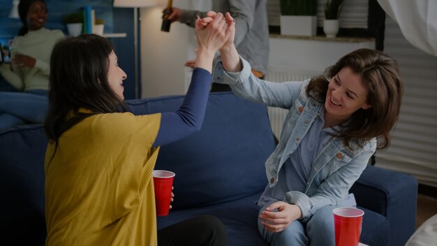 vrolijke vrouwen vieren vriendschap met high five 's avonds laat in de woonkamer