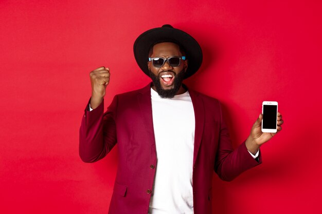 Vrolijke winnende zwarte man met smartphone-scherm