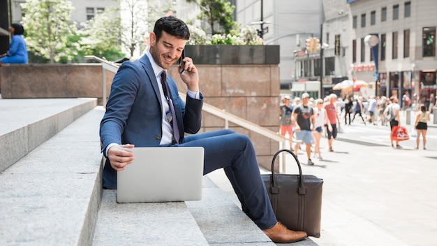 Vrolijke zakenman die op telefoon spreekt en laptop met behulp van