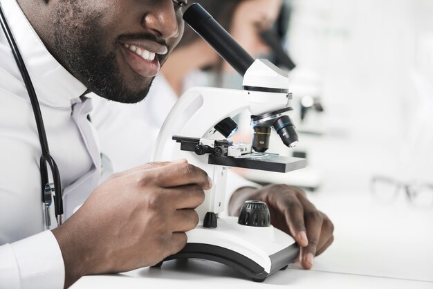 Vrolijke zwarte dokter met behulp van de microscoop