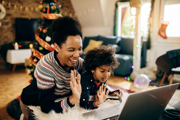 Vrolijke zwarte moeder en dochter begroeten iemand tijdens videogesprek met Kerstmis