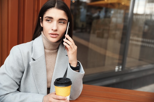 Vrouw achter café zitten en praten op mobiele telefoon. Zakenvrouw praten met de klant tijdens het werken vanuit een café.