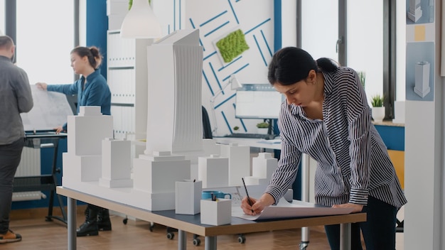 Vrouw architect analyseert blauwdrukken plan op tafel om bouwmodel en maquette te ontwerpen. Ingenieur bezig met architectonisch ontwikkelingsproject met industriële bouwhulpmiddelen.