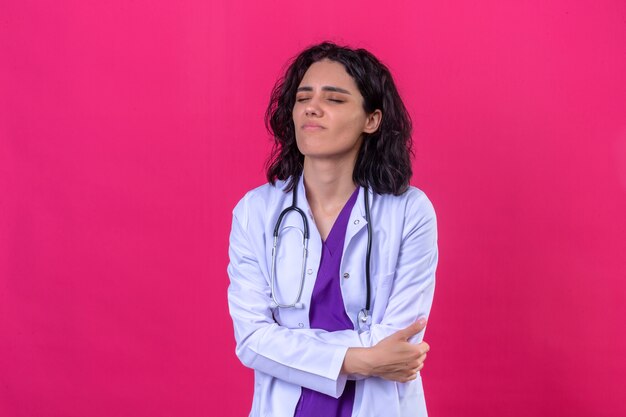 vrouw arts die witte jas met een stethoscoop draagt die onwel kijkt grijpende buik met buikpijn die zich op geïsoleerde roze bevindt