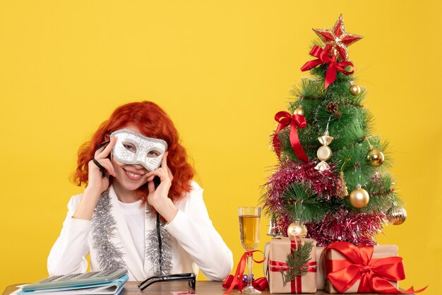 vrouw arts masker dragen rond kerstboom en presenteert op geel