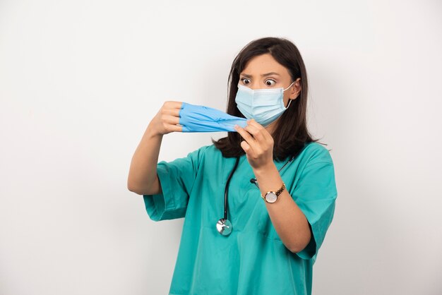 Vrouw arts met de medische handschoenen van de maskerholding op witte achtergrond.