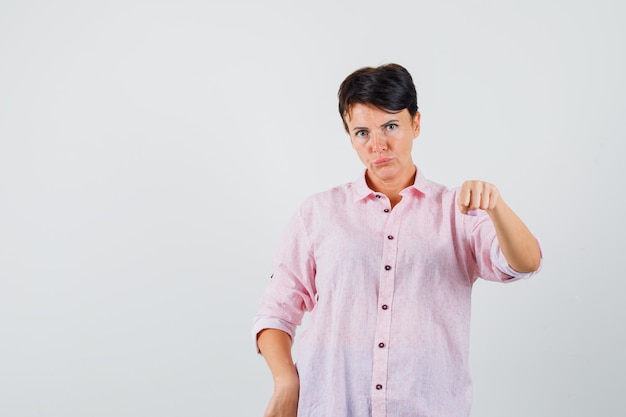 Vrouw bedreigt met vuist in roze shirt en kijkt streng. vooraanzicht.