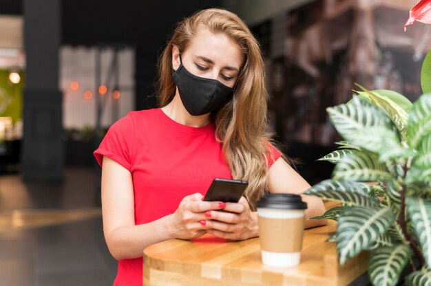 Vrouw bij wandelgalerij met masker mobiel controleren