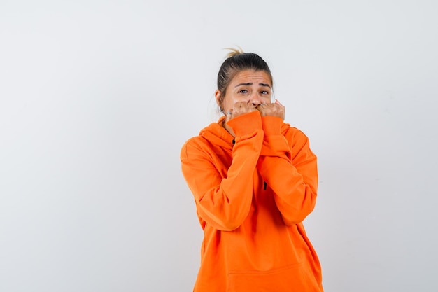 Vrouw bijt emotioneel vuisten in oranje hoodie en kijkt bang