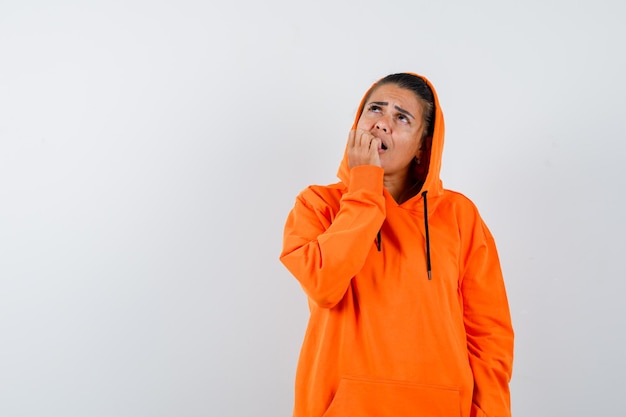 Gratis foto vrouw bijt op haar nagels in oranje hoodie en kijkt bang