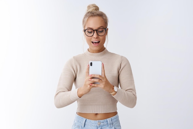 Vrouw blogger die foto maakt via smartphone en geamuseerd blij gezicht maakt lachend leuk vinden om mobiele telefoon op wit te fotograferen