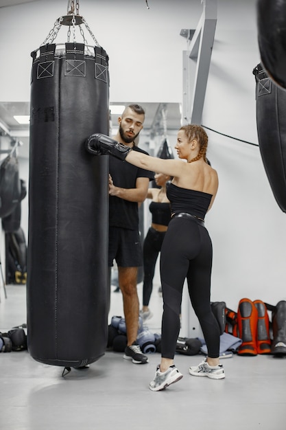 Vrouw boksen. Beginner in een sportschool. Dame in zwarte sportkleding. Vrouw met coach.