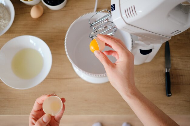 Vrouw breekt kippeneieren in een kom in de keuken.