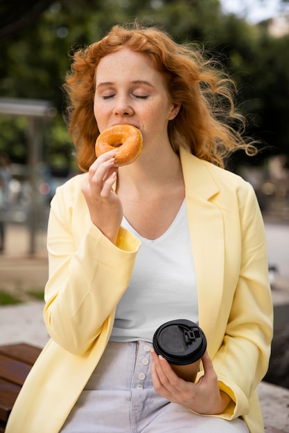 Vrouw buiten genieten van een lekkere donut en een kopje koffie