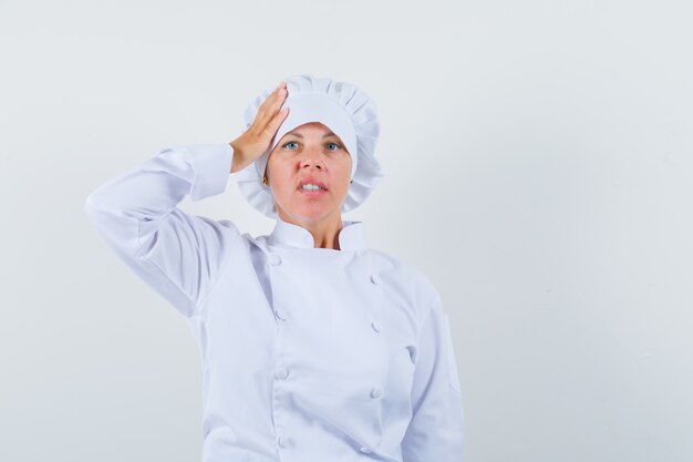 vrouw chef-kok die hand op het hoofd in wit uniform en op zoek attent.