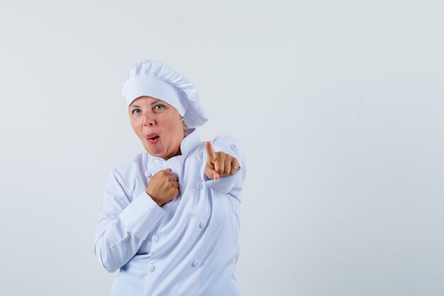 vrouw chef-kok in wit uniform wijzend naar voren met een hand op de borst en kijkt verbaasd