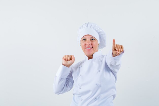 vrouw chef wijst naar voren terwijl ze haar vuist in wit uniform toont