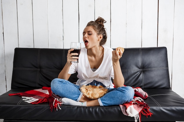 vrouw chips eten, frisdrank drinken, tv kijken, zittend op de bank.