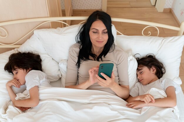 Vrouw controleert haar smartphone terwijl haar tweeling slaapt