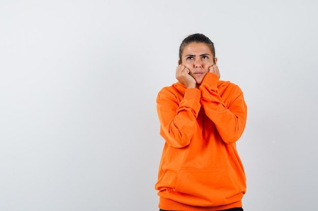 vrouw dempt gezicht op haar handen in oranje hoodie en kijkt peinzend